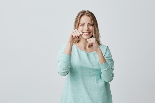 felice vincitore di successo giovane donna bionda vestita casualmente mantenendo i pugni chiusi mentre tifo e sentirsi fortunati