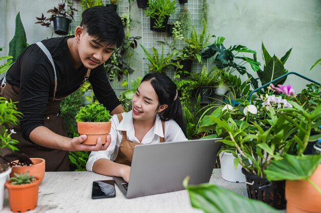 Felicemente coppia di giardinieri usa il computer portatile mentre tutorial online sui piani in vaso in officina insieme