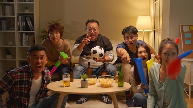 Felici amici asiatici o tifosi di calcio che guardano il calcio in tv e festeggiano la vittoria a casa