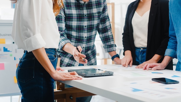 Felici giovani uomini d'affari asiatici e imprenditrici che incontrano idee di brainstorming su nuove scartoffie colleghi di progetto che lavorano insieme pianificando una strategia di successo godono del lavoro di squadra in un piccolo ufficio moderno.