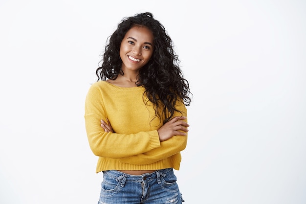 Felicità, benessere e concetto di fiducia. Taglio di capelli ricci donna afroamericana attraente allegra, petto a braccia incrociate in posa potente e sicura di sé, sorridente determinato, indossa un maglione giallo