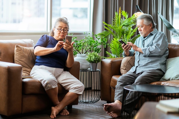 Felicità coppia in pensione asiatica godere di giocare e gioco di concorrenza smartphone mobile online insieme sul divano in soggiorno interno casa coppia asiatica che gioca gioco insieme casa isolare idea