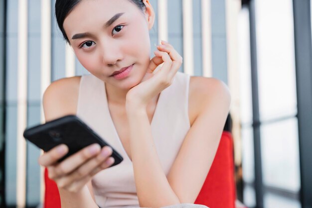 Felicità della donna asiatica attraente dell'ufficio e comunicazione gioiosa con il cliente sullo sfondo dell'ufficio dello smartphone