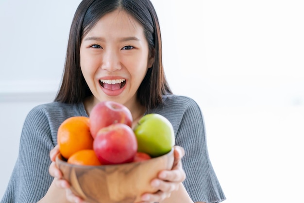 Felicità sana e bella di sorriso della donna asiatica con la ciotola della dieta della frutta fresca e mangiare il concetto sano di idee di buona nutrizione