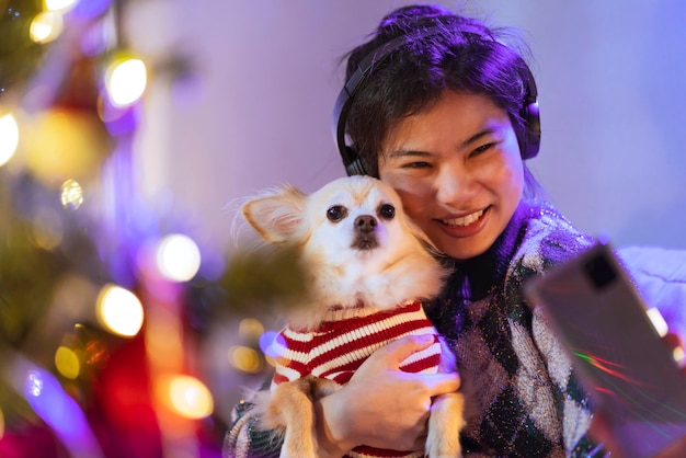 Felicità stile di vita con animale donna asiatica sorridente dogfriendly tenere piccolo cucciolo cagnolino mentre ascolta musica in cuffia wnjoy natale capodanno vacanza weelend di notte festeggiando se stessa