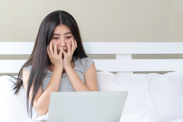 Femmina adolescente asiatica che si siede sul letto e che guarda film dal computer portatile