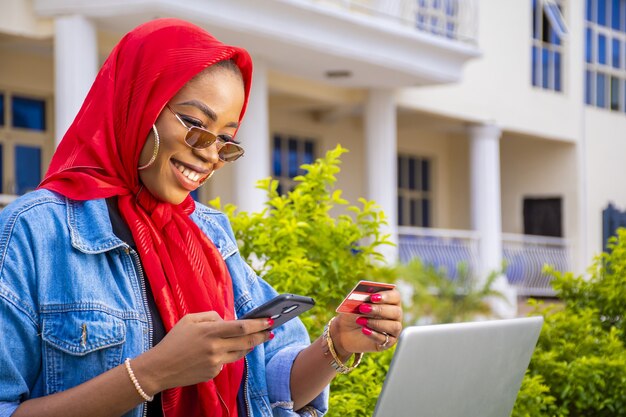 Femmina africana felicemente lo shopping online utilizzando un laptop e uno smartphone mentre si tiene la sua carta di credito