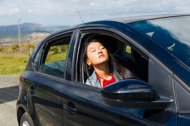 Femmina asiatica che si siede in macchina e che gode del sole