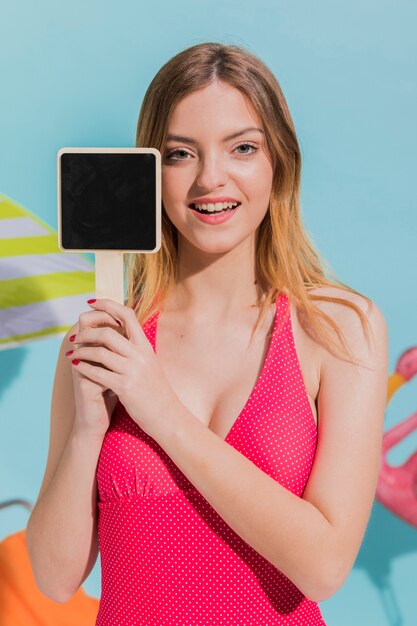 Femmina attraente in costume da bagno che tiene segno in bianco