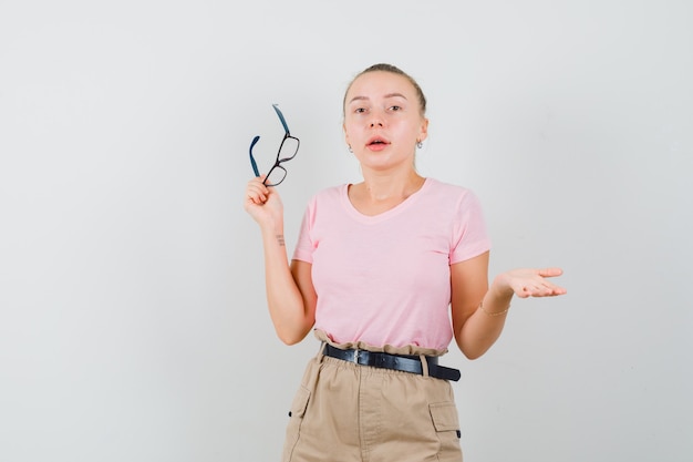 Femmina bionda in t-shirt, pantaloni con gli occhiali e guardando confuso, vista frontale.