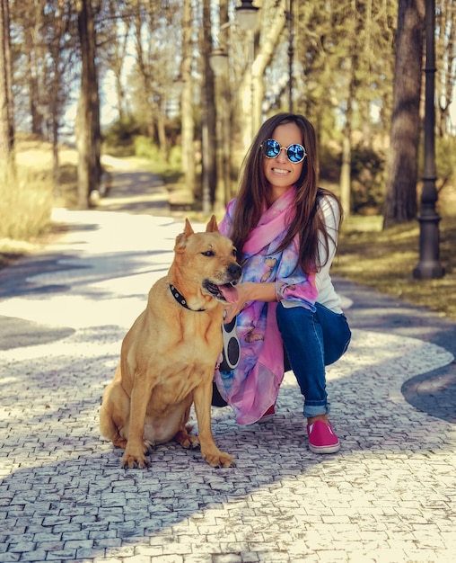 Femmina casuale sorridente con il suo cane marrone pitbull in un parco.