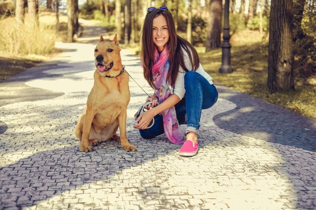 Femmina casuale sorridente con il suo cane marrone pitbull in un parco.