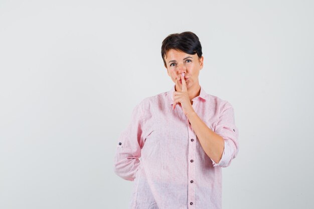 Femmina che mostra gesto di silenzio in camicia rosa e guardando attento, vista frontale.