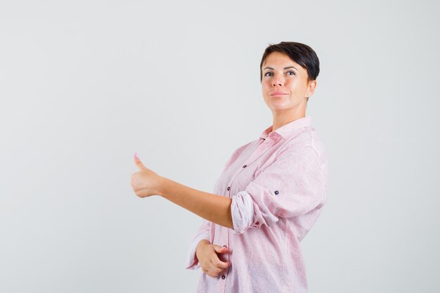 Femmina che mostra il pollice in su in camicia rosa e sembra sicura.