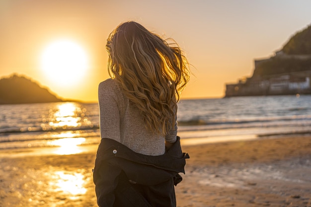 Femmina che si toglie il cappotto mentre si cammina verso il mare al tramonto
