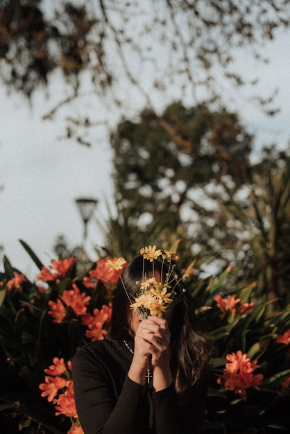 Femmina che tiene un mazzo dei wildflowers davanti al suo fronte in un giardino con uno sfondo naturale