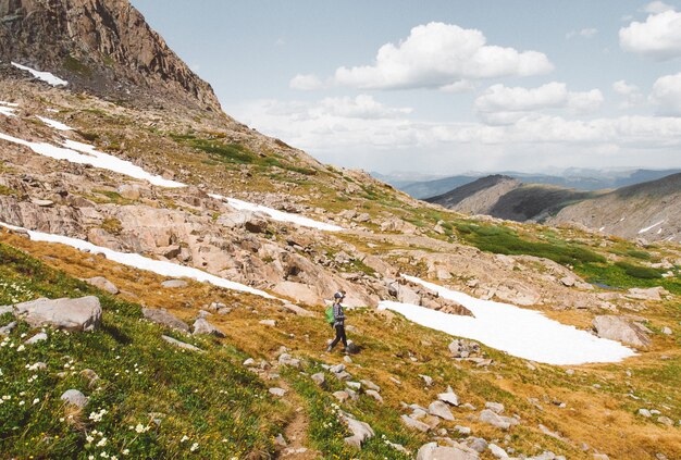 Femmina con uno zaino che fa un'escursione giù una montagna sotto un cielo nuvoloso al giorno