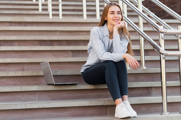 Femmina di angolo basso sulle scale con il computer portatile accanto