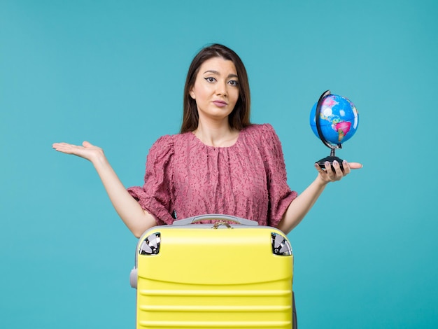 Femmina di vista frontale in vacanza che tiene il piccolo globo della terra sulla donna di estate di viaggio di viaggio di vacanza del mare dello scrittorio blu