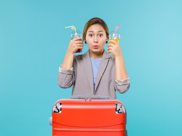 Femmina di vista frontale in vacanza che tiene le bevande fresche sull'aereo di mare di viaggio di viaggio di viaggio di viaggio di sfondo azzurro