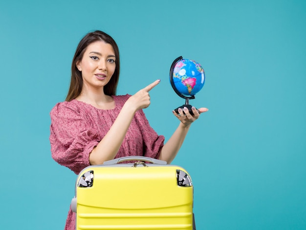 Femmina di vista frontale in vacanza che tiene piccolo globo della terra sull'estate di viaggio di viaggio della donna di vacanza del mare del fondo blu