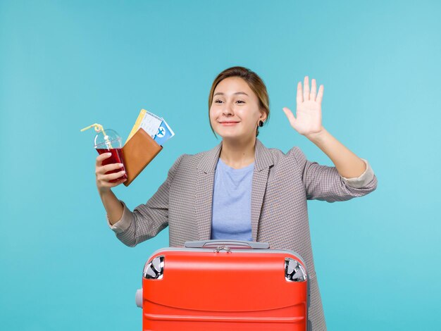 Femmina di vista frontale in vacanza che tiene succo e biglietti salutando qualcuno su sfondo blu viaggio vacanza viaggio viaggio idrovolante