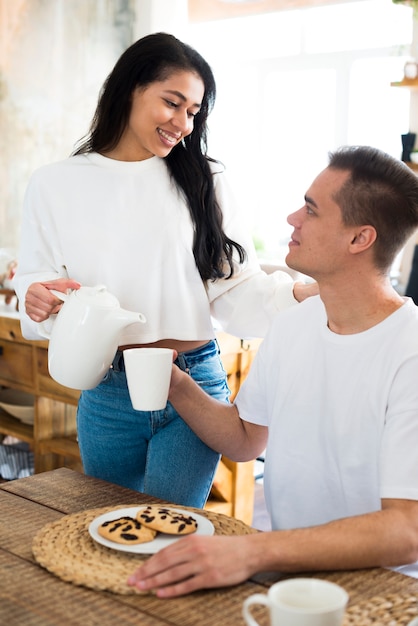 Femmina etnica sorridente che versa in tazza per il ragazzo