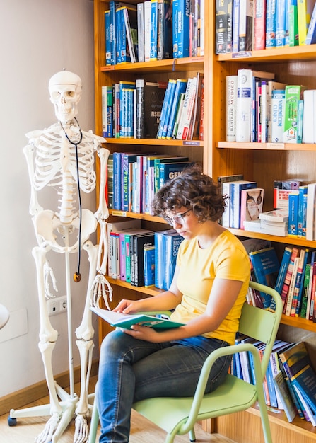 Femmina geek sulla sedia seduta con il libro