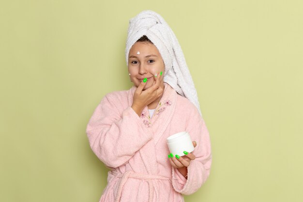 femmina in accappatoio rosa utilizzando una crema per il viso