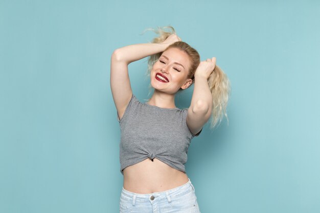 femmina in camicia grigia e blue jeans luminosi sorridendo e toccandosi i capelli