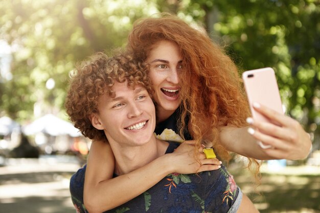 Femmina positiva che abbraccia il suo ragazzo e che tiene il telefono cellulare