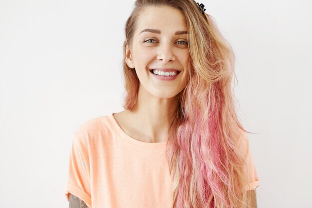 Femmina positiva con i capelli lunghi, indossa abiti casual, sorride piacevolmente mostrando i suoi denti perfetti