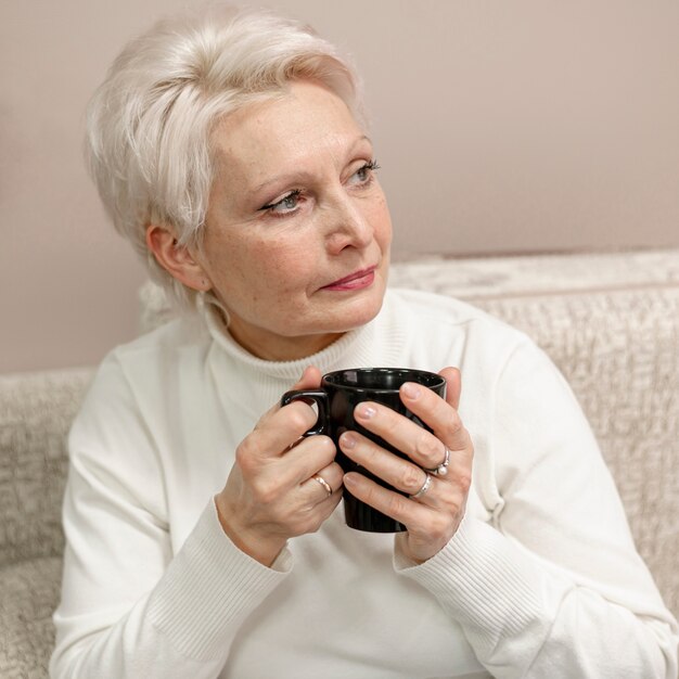Femmina senior dell'angolo alto a casa che beve caffè