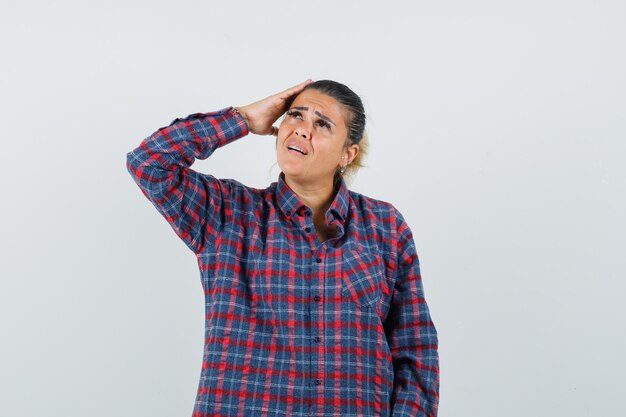 Femmina tenendo la mano sulla testa in camicia casual e guardando malinconico. vista frontale.