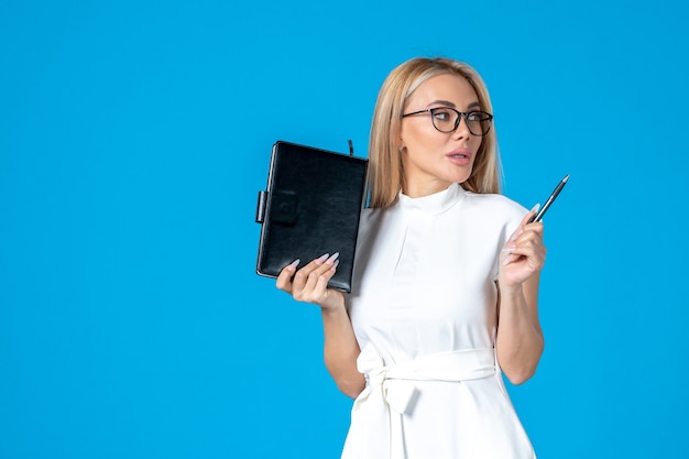 Femmina vista frontale in abito bianco in posa con blocco note sull'autorità di lavoro blu