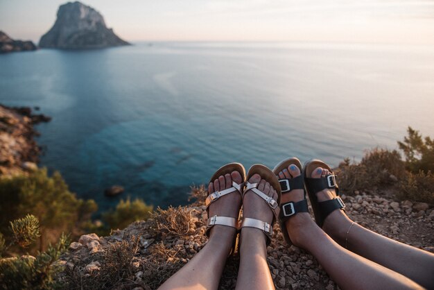 Femmine sedute su una scogliera in riva al mare che si godono la splendida vista del tramonto