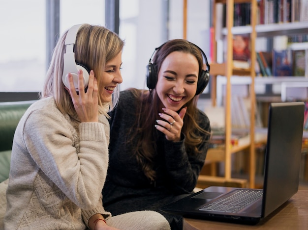 Femmine sorridenti che indossano le cuffie che esaminano computer portatile