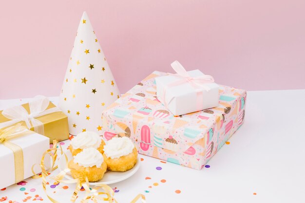 Festa di compleanno con cupcake; scatole regalo e cappello da festa sulla scrivania bianca