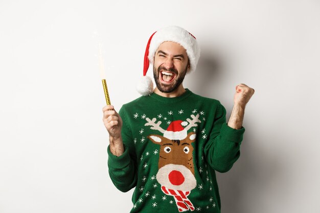 Festa di Natale e concetto di vacanze. Felice giovane che festeggia il capodanno natale, tiene in mano una scintilla e sembra eccitato, in piedi su sfondo bianco