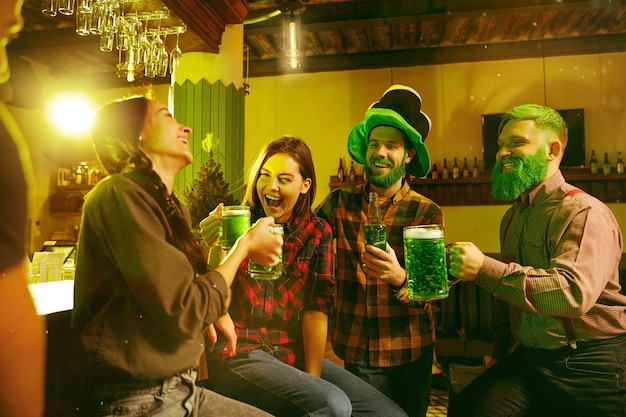 Festa di San Patrizio. Amici felici festeggia e beve birra verde. Giovani uomini e donne che indossano cappelli verdi. Pub interno.