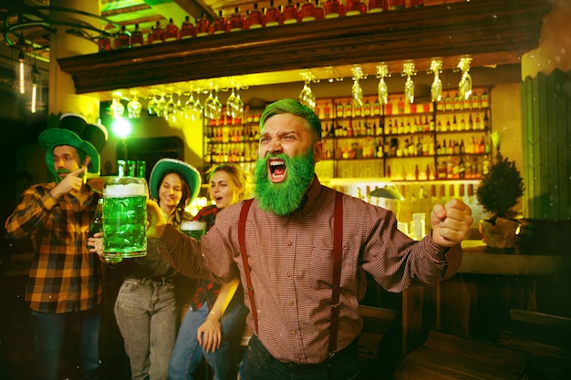 Festa di San Patrizio. Amici felici festeggia e beve birra verde. Giovani uomini e donne che indossano cappelli verdi. Pub interno.