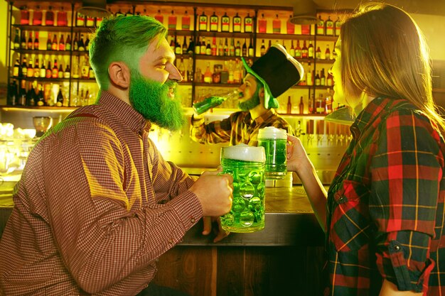 Festa di San Patrizio. Gli amici felici stanno festeggiando e bevendo birra verde. Giovani uomini e donne che indossano cappelli verdi. Pub interno.