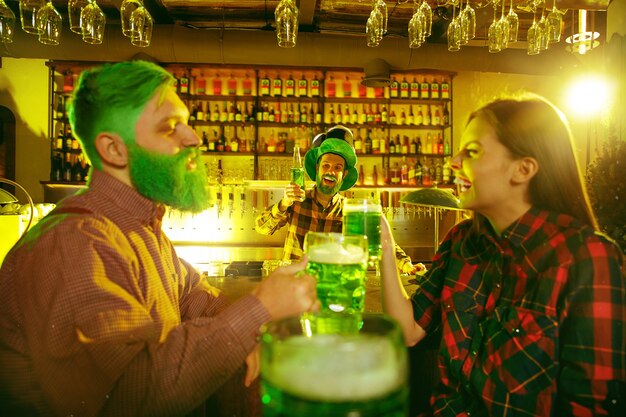 Festa di San Patrizio. Gli amici felici stanno festeggiando e bevendo birra verde. Giovani uomini e donne che indossano cappelli verdi. Pub interno.