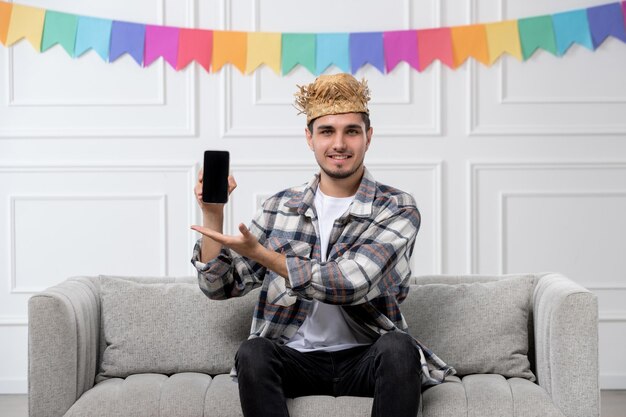 Festa junina bel ragazzo adorabile con cappello di paglia e camicia che celebra il festival con il telefono nero