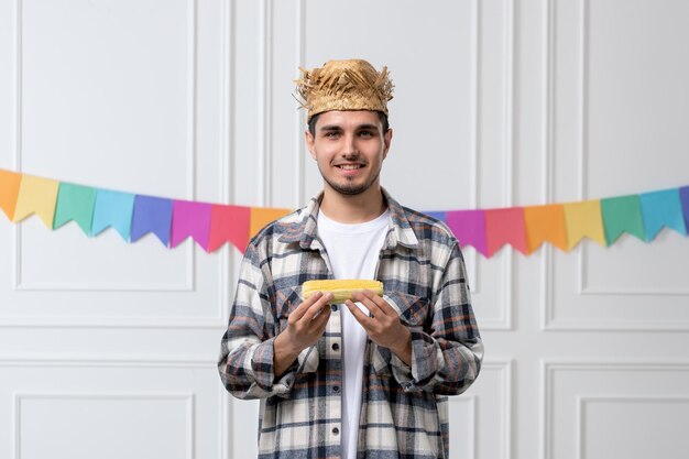 Festa junina bel ragazzo adorabile in camicia con cappello di paglia che celebra il festival mangiando mais