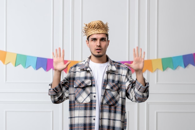 Festa junina bel ragazzo adorabile in camicia con cappello di paglia che celebra il festival spaventato mani in alto