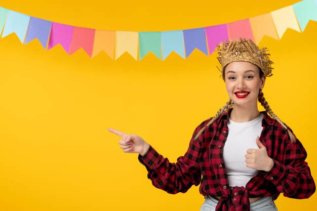 Festa junina bionda ragazza carina in cappello di paglia festival brasiliano con bandiere colorate che punta il dito