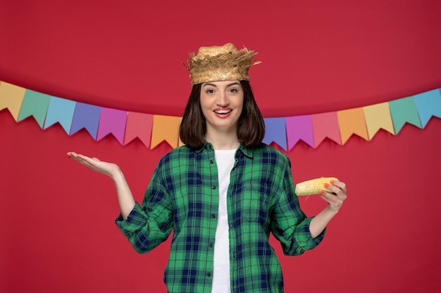 Festa junina felice ragazza carina che indossa un cappello di paglia che celebra il festival brasiliano tenendo il mais