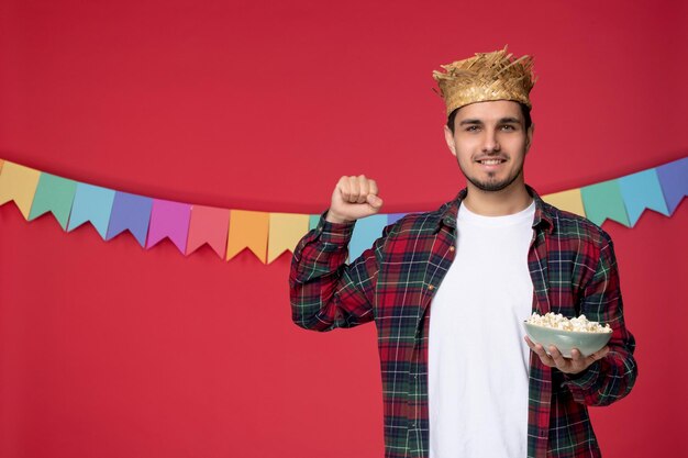 Festa junina felice ragazzo carino che indossa un cappello di paglia che celebra il festival brasiliano mangiando popcorn