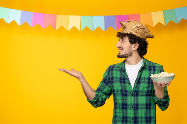 Festa junina giovane ragazzo carino con cappello di paglia e bandiere colorate festival brasiliano che tiene popcorn